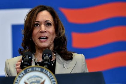 Kamala Harris speaking at a campaign rally with supporters in the background.